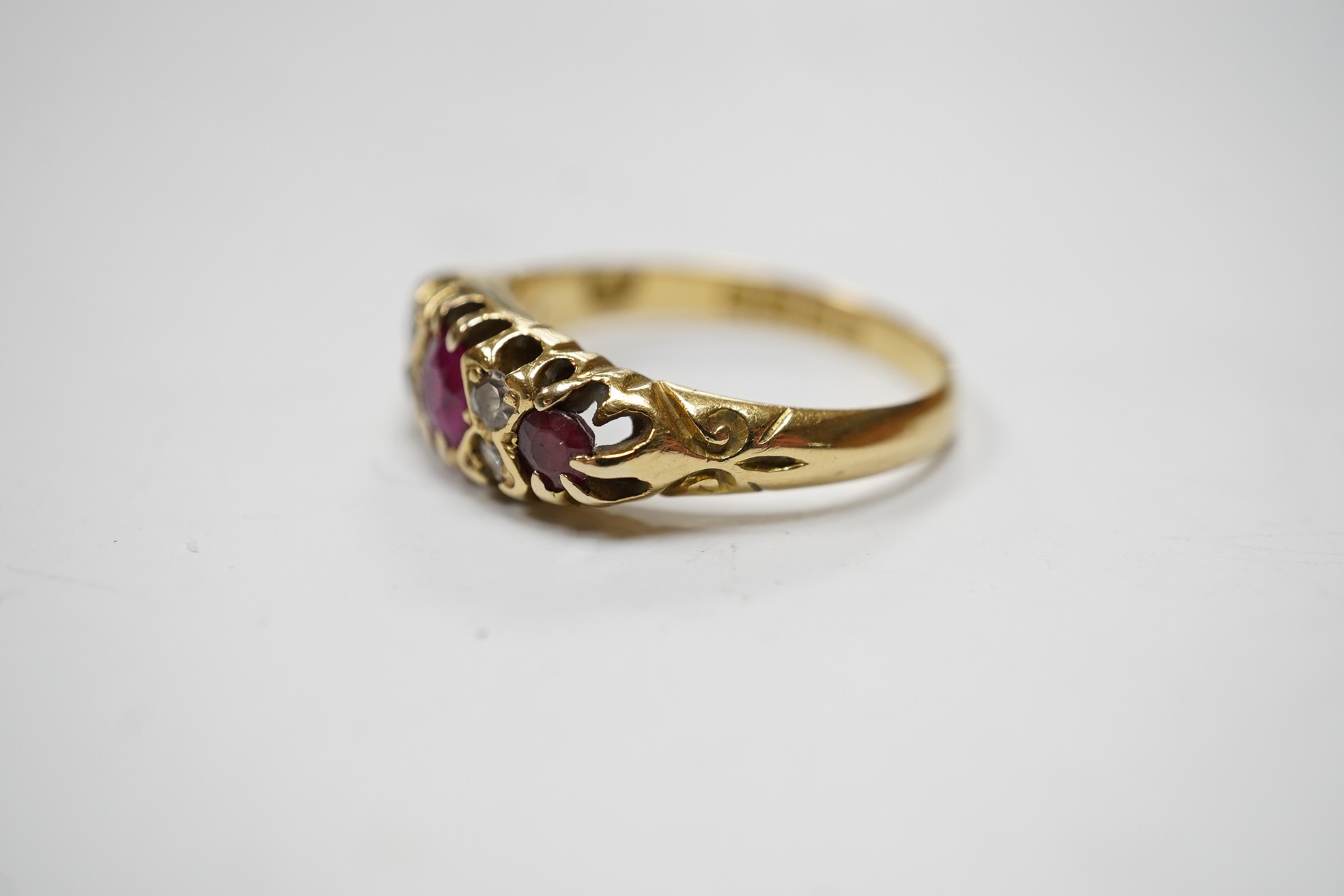 A George V 18ct gold and three stone ruby set half hoop ring, with diamond chip spacers, (one stone is probably a paste replacement), size O, gross weight 3.8 grams. Condition - poor to fair.